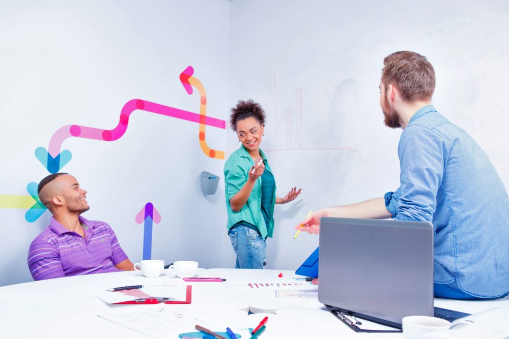 Creative brainstorming. Group of cheerful business people in smart casual wear discussing infographics and writing on the board in the meeting room